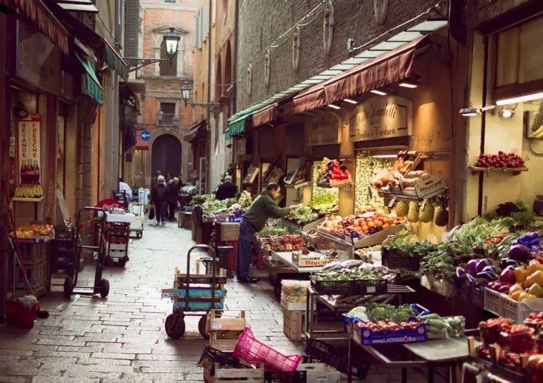 Obst- und Gemüsestände unter Markisen in einer engen Gasse des Quadrilatero in Bologna