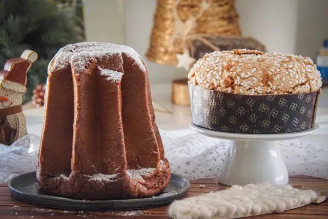 Ein mit Zucker bestäubter Pandoro neben einem Panettone mit Mandelglasur und Hagelzucker