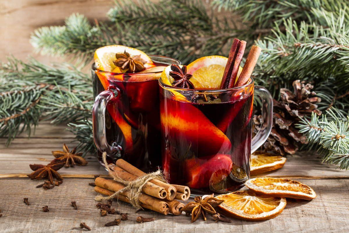 Zwei Gläser Glühwein mit Orangenscheiben, Sternanis und Zimtstangen zwischen Tannenzweigen