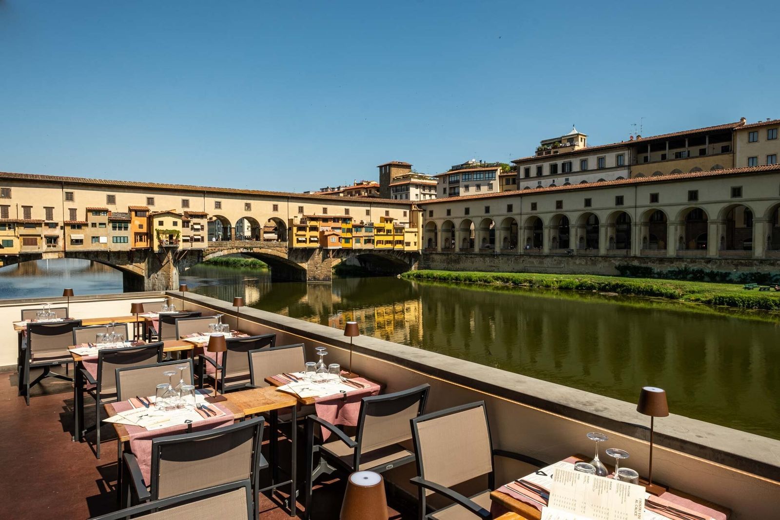 Tables laid on a terrace above the Arno, facing the Ponte Vecchio and the arcaded riverfront of the Vasari Corridor