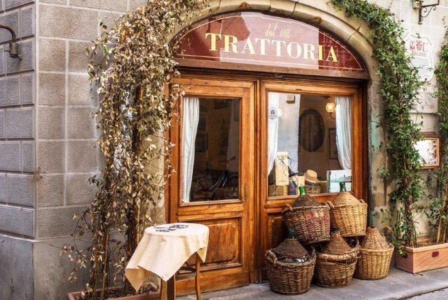 The wooden doorway of an old trattoria, wicker-wrapped demijohns stacked beside a small table outside