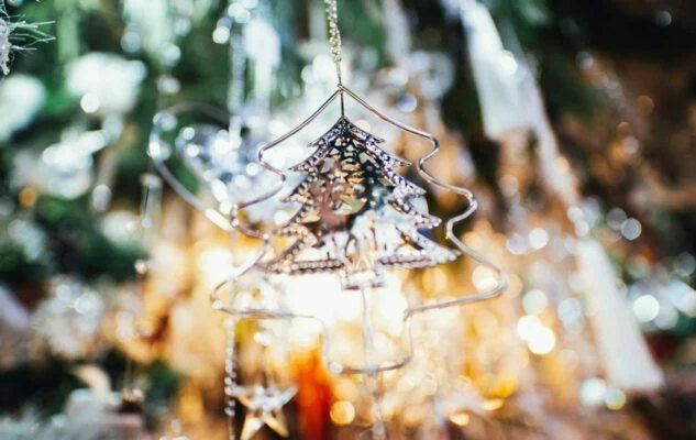 A silver ornament shaped like a Christmas tree, hanging against soft, blurred lights