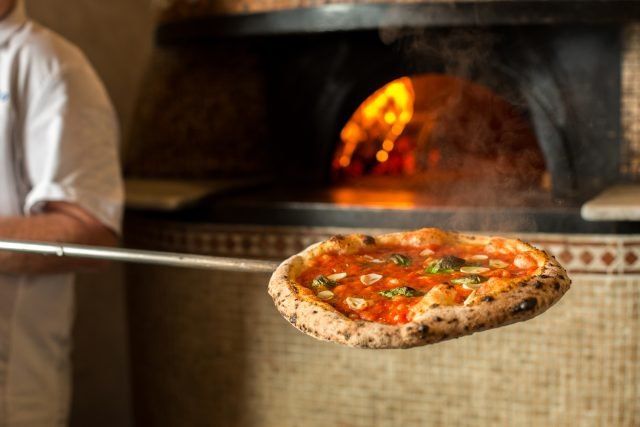 A just-baked pizza on a peel in front of a wood-fired oven