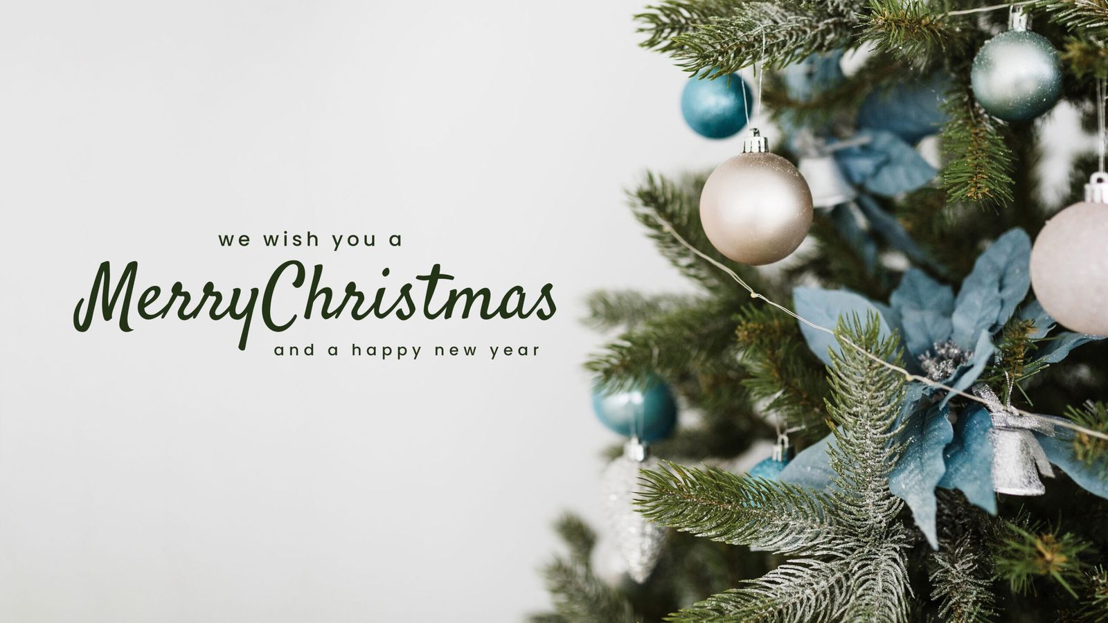 Ein Weihnachtsbaum mit blauen, silbernen und weißen Kugeln neben dem englischen Schriftzug „We wish you a Merry Christmas and a happy new year“