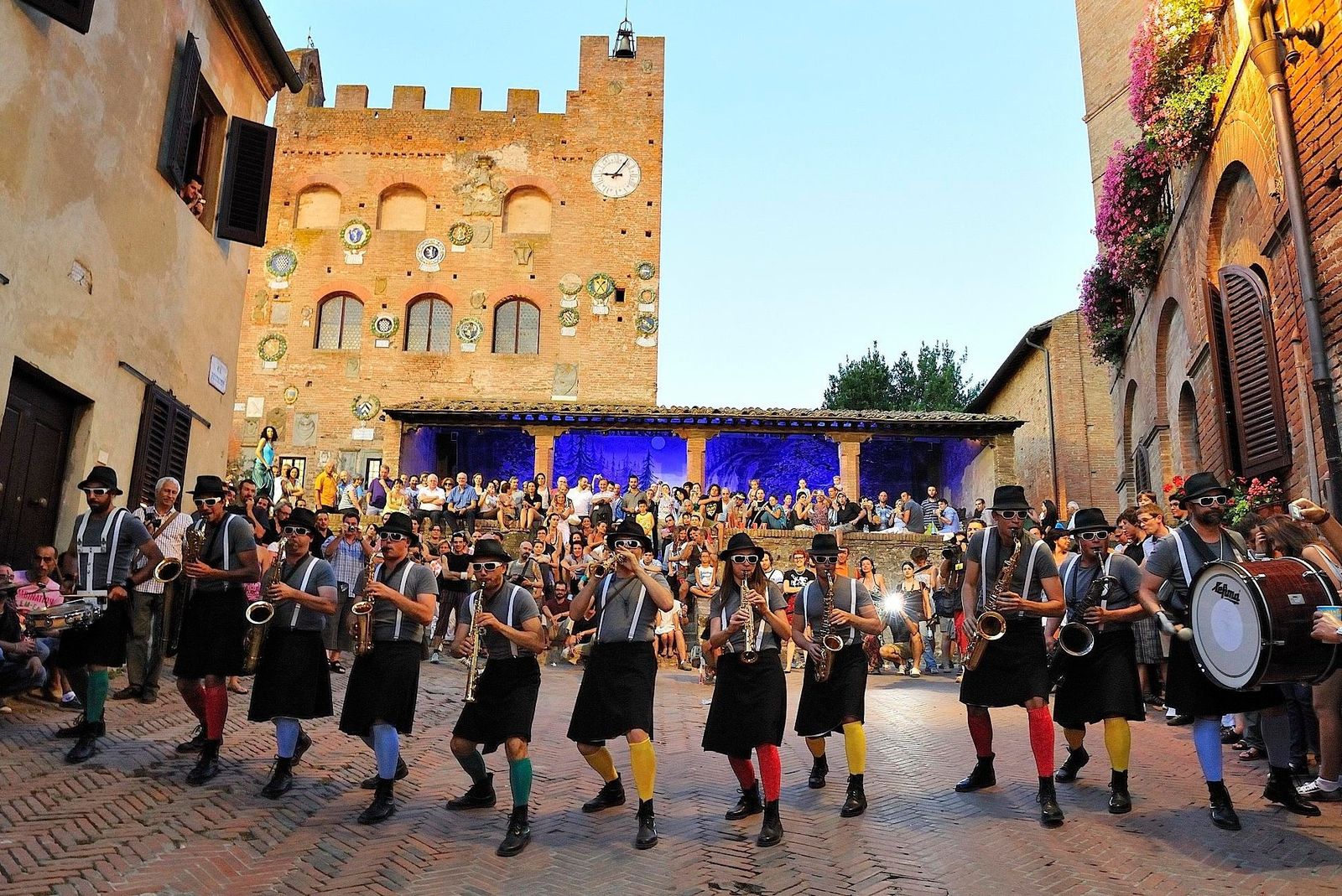 A street band with saxophones and a bass drum playing to a crowd before the Palazzo Pretorio in Certaldo Alto, Tuscany, on a summer evening