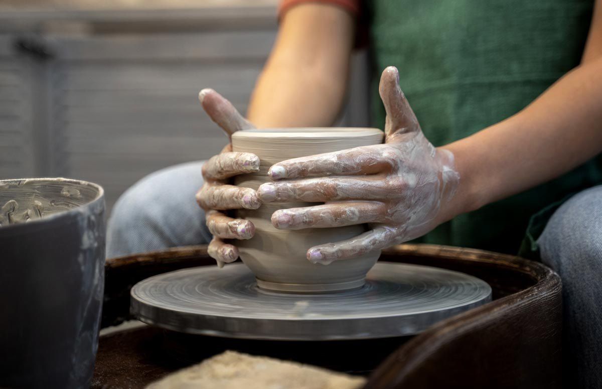 Clay-covered hands shaping a pot on a potter’s wheel