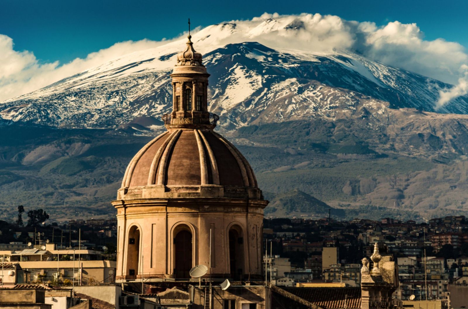 La cúpula de una iglesia barroca de Catania, con el Etna nevado alzándose tras la ciudad
