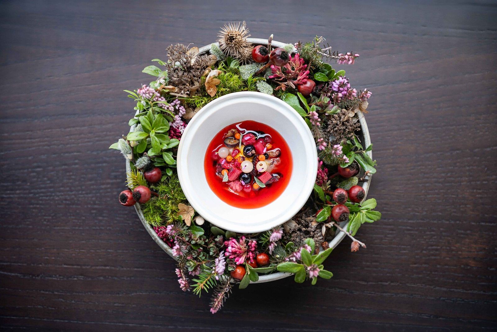 A dessert of mountain berries in a ruby-red syrup, served in a white bowl set in a ring of moss, heather and rosehips