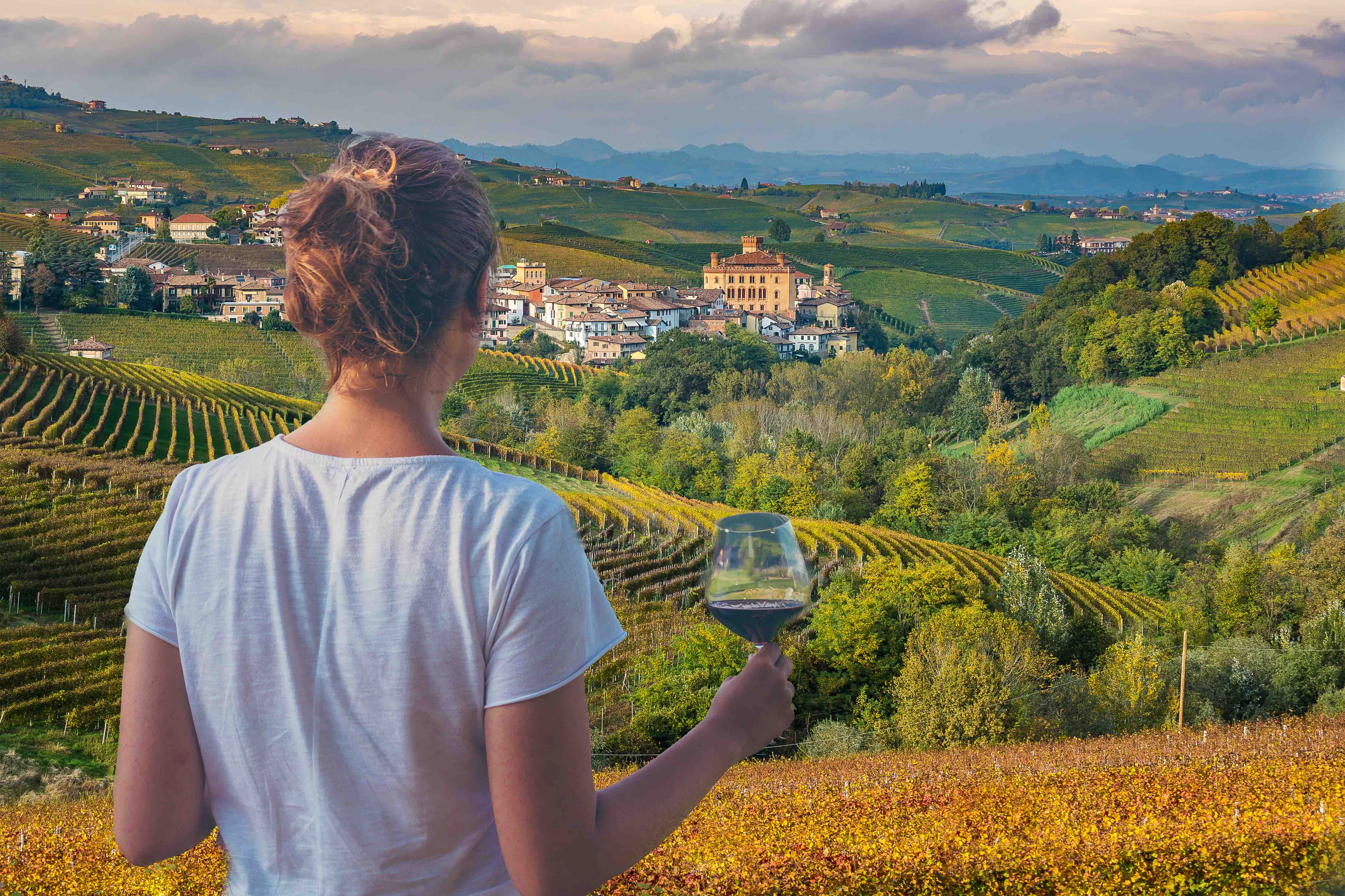 Frau mit einem Glas Rotwein, die die Landschaft und die Weinberge in Italien betrachtet.